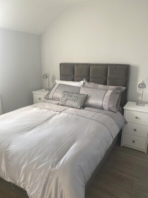 Un dormitorio con cama, mesitas de noche y cabecero.