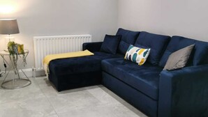 A modern living room with a dark blue sectional sofa, a yellow throw blanket, and a lamp on a side table.