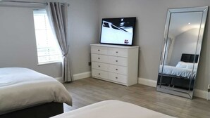 A modern bedroom with two beds, a TV, a dresser, and a large mirror.