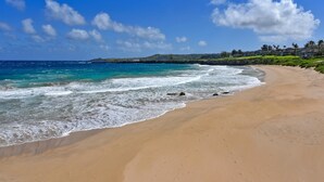 A beach with clear blue water, a sandy shore, and a distant view of houses and greenery. - Kapalua Bay Villa 29b4 1 Bedroom Villa by RedAwning (Lahaina)