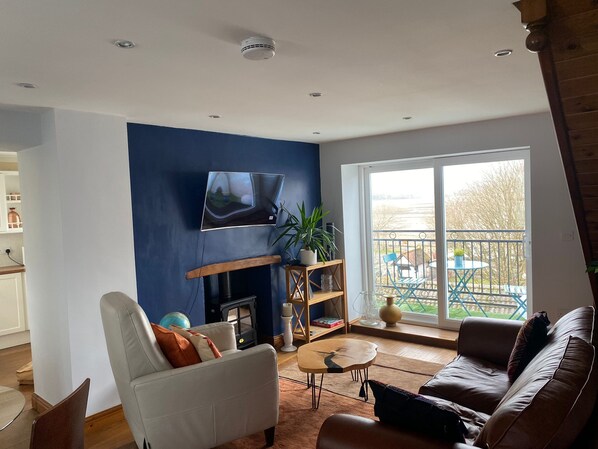 A living room with a fireplace, a television mounted on the wall, a sofa, a coffee table, and a view of the outside balcony.