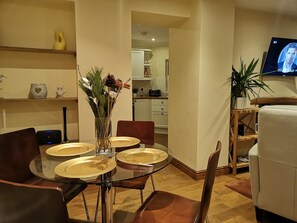 A modern living room with a dining area, featuring a glass table, brown leather chairs, and a vase with dried flowers.