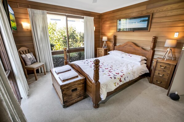 Une chambre à coucher aux murs lambrés, avec un lit, des tables de chevet, une chaise et une fenêtre avec des rideaux.