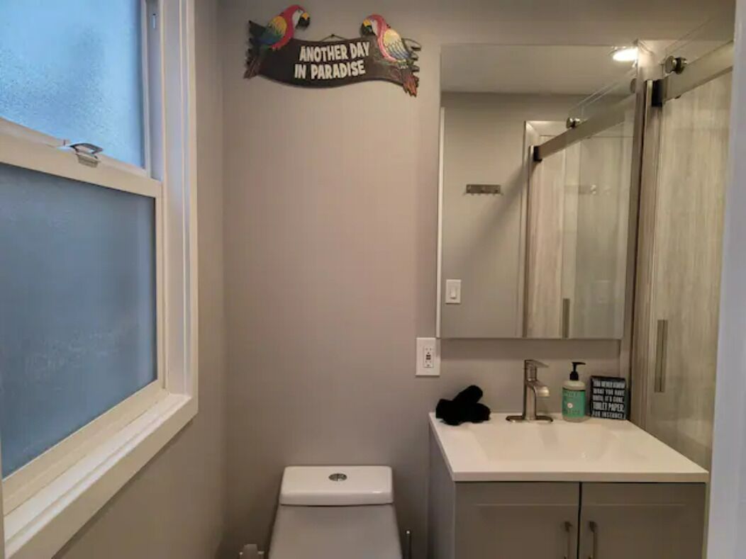 Un bagno con il water, lavandino e specchio. Un cartello al muro recita: 'Un altro giorno in paradiso'.