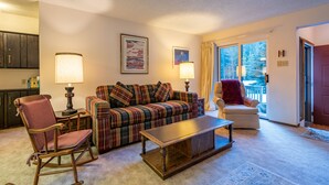 A living room with a plaid sofa, a rocking chair, a coffee table, and a door leading to a balcony. - Cozy Ski-in/Walk-out condo, free wifi, & parking, great deck (Copper Mountain)
