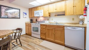 A kitchen with wooden cabinets, a microwave, an oven, a dishwasher, and a dining table with chairs. - Cozy Ski-in/Walk-out condo, free wifi, & parking, great deck (Copper Mountain)