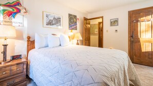 A bedroom with a large bed, two bedside tables with lamps, a wooden door, and wall decorations including posters and a framed picture. - Cozy Ski-in/Walk-out condo, free wifi, & parking, great deck (Copper Mountain)