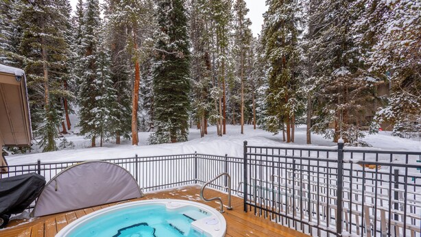 An outdoor hot tub on a wooden deck with a metal railing, surrounded by snow-covered trees. - Cozy Ski-in/Walk-out condo, free wifi, & parking, great deck (Copper Mountain)