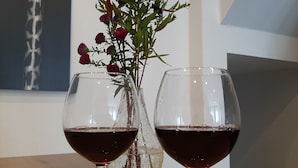 Two wine glasses filled with red wine on a wooden table, with a vase of purple and red flowers in the background. - Vacation cottage Am Mühlengraben (Merchweiler)
