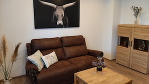 A living room with a brown leather sofa, a wooden coffee table, and a cabinet with a Buddha statue. - Vacation cottage Am Mühlengraben (Merchweiler)