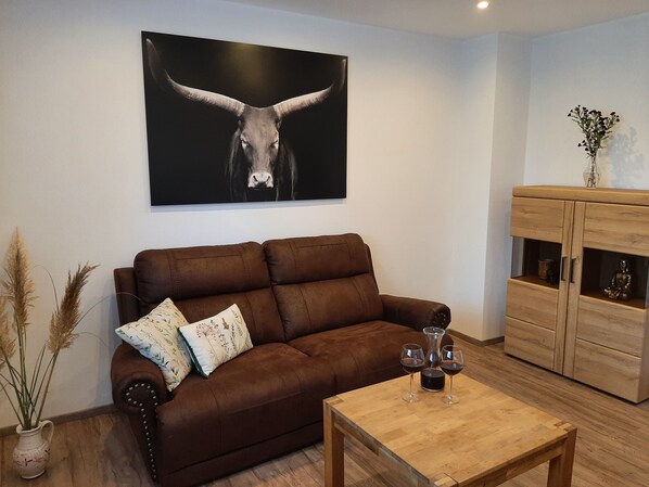 A living room with a brown leather sofa, a wooden coffee table, and a cabinet with a Buddha statue. - Vacation cottage Am Mühlengraben (Merchweiler)