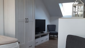 A modern, well-lit room with a large wardrobe, a television on a stand, a grey armchair, and a small white table. - Vacation cottage Am Mühlengraben (Merchweiler)