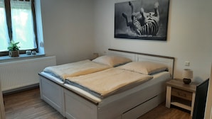 A double bed with a headboard, a bedside table with a lamp, a radiator, a window with curtains, and a wall-mounted zebra painting. - Vacation cottage Am Mühlengraben (Merchweiler)