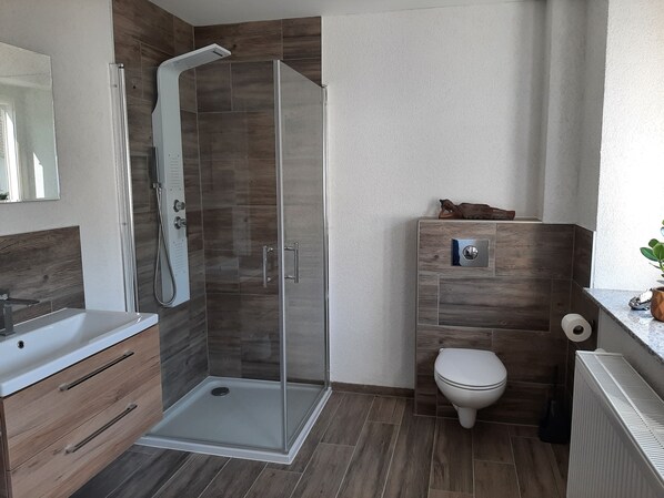 A modern bathroom with a glass-enclosed shower, a wooden vanity, a toilet, and a radiator.