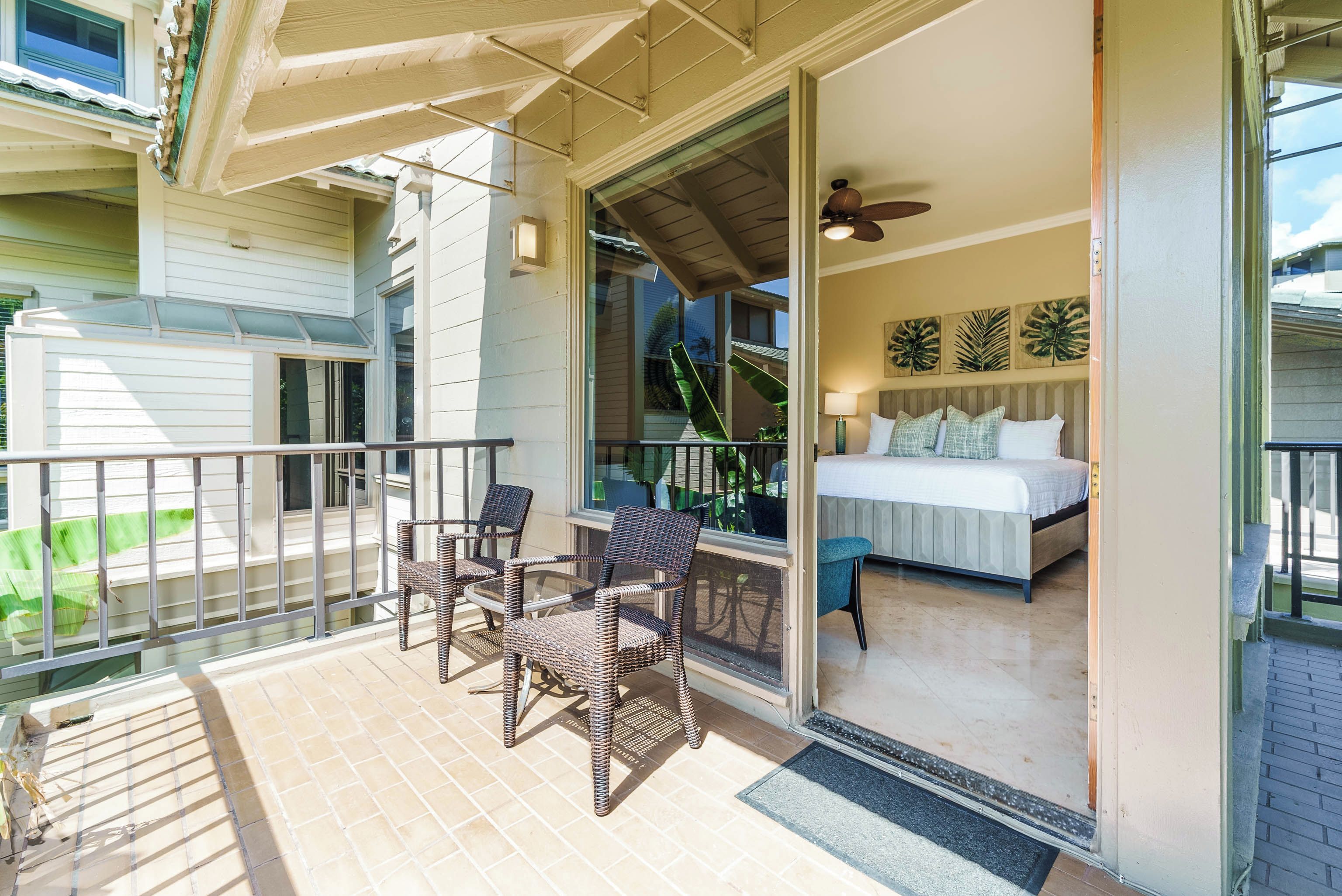 A balcony with wicker chairs and a bed with a white bedspread and pillows.