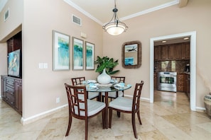 A dining area with a round table, chairs, a vase, and framed artwork on the wall.