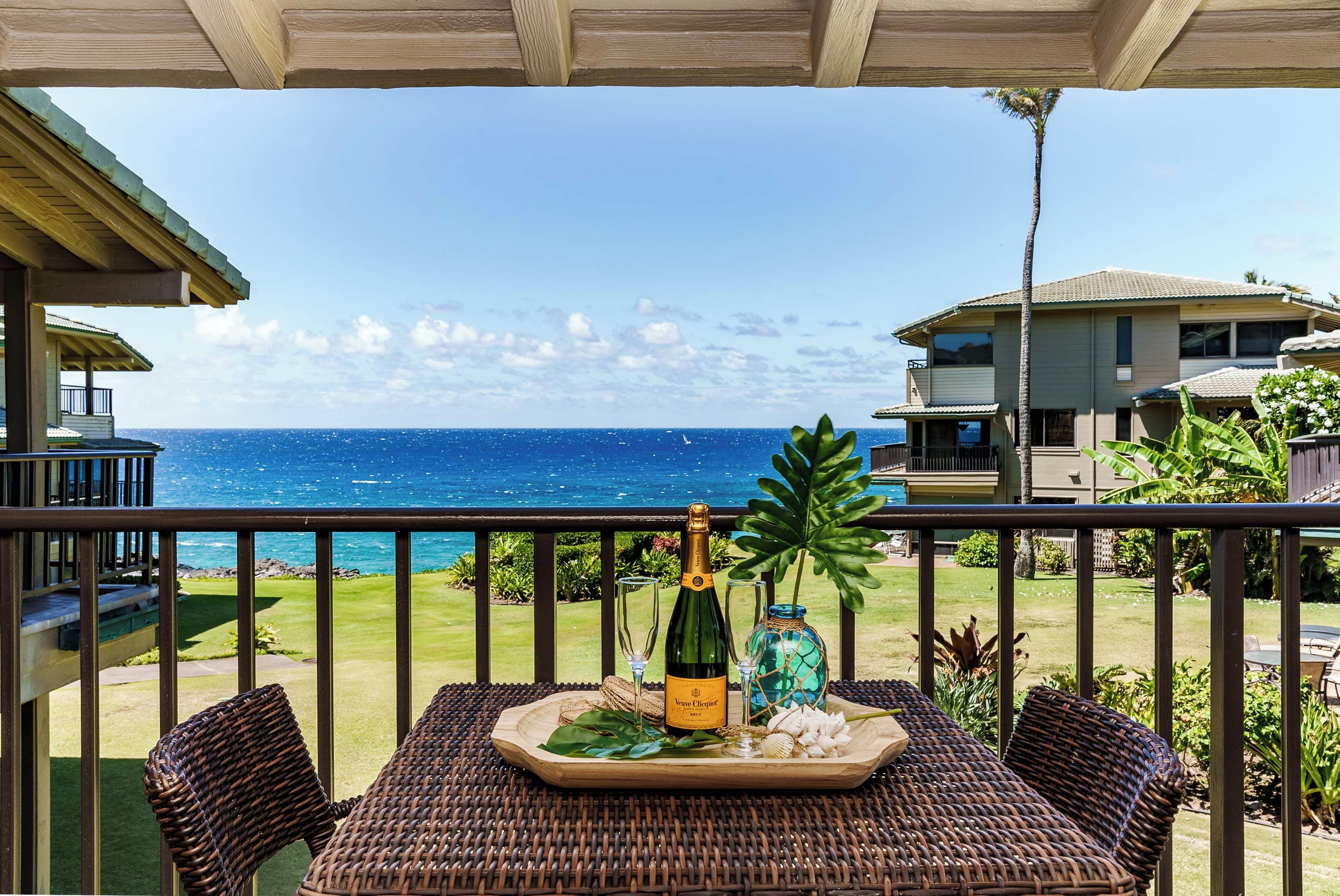 Un balcon avec vue sur l’océan, une bouteille de champagne et un plateau avec un verre et un objet décoratif.
