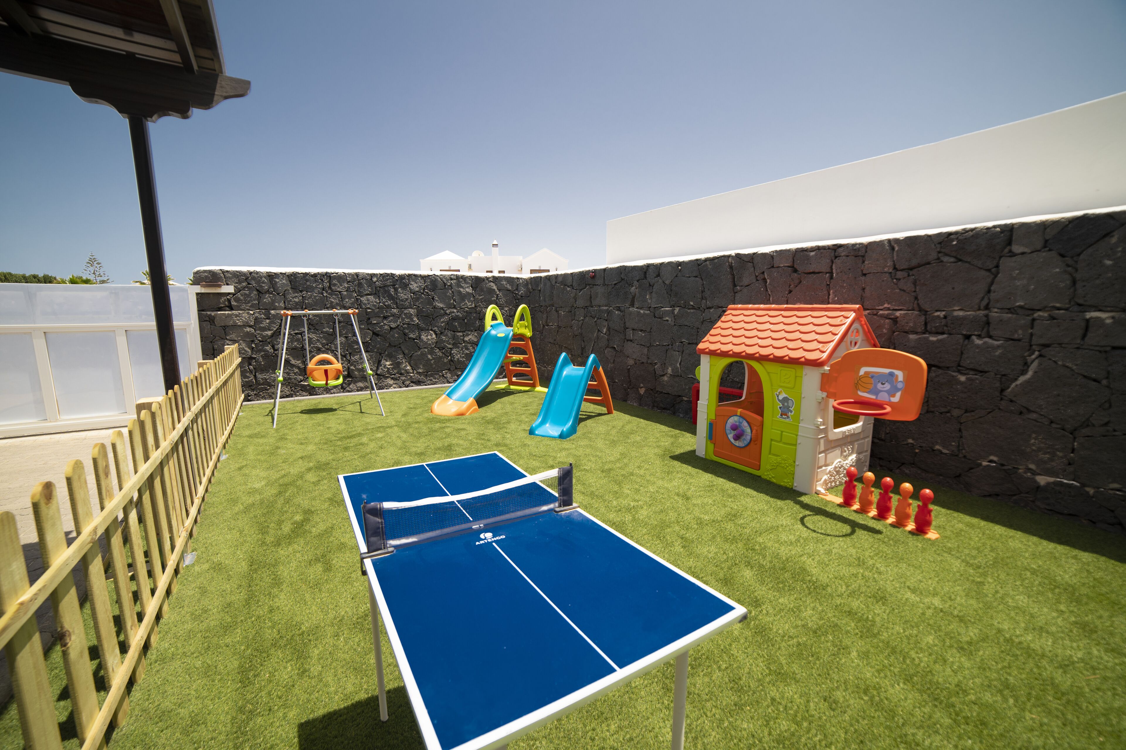 A children's play area with a ping pong table, slides, and a small basketball hoop.
