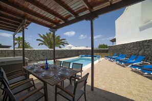 A poolside area with a covered dining table, lounge chairs, and a view of a swimming pool. - Private pool and hot tub, mountain and sea views, pool table, children’s park. (Playa Blanca)