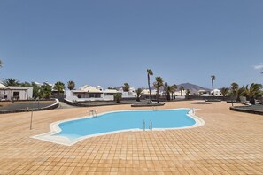 Une piscine dotée d’une terrasse carrelée, entourée de palmiers et de bâtiments.