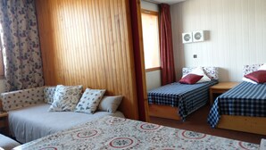 Et værelse med sofa, to enkeltsenge, et træskab og et vindue med gardiner.