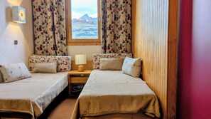 A room with two single beds, a wooden desk with a lamp, and a window with curtains. - Studio center resort beautiful view Les Coches La Plagne Paradiski (Bellentre)