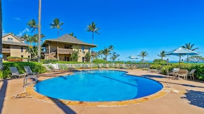 Área de piscina do resort com piscina azul cristalina, cadeiras de descanso e vista para o oceano.