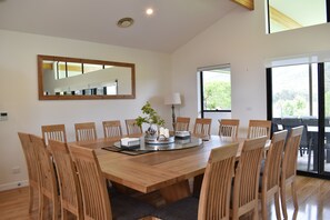 A spacious dining area with a large wooden table surrounded by chairs, a mirror on the wall, and a window providing a view of greenery outside.