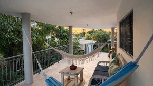 Ein Balkon mit einer Hängematte, einem kleinen Tisch mit einer Pflanze und einer Couch mit Kissen.