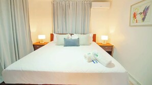 Ein Hotelzimmer mit einem großen Bett, zwei Nachttischen mit Lampen, einem Deckenventilator und einem Fenster mit Vorhängen.