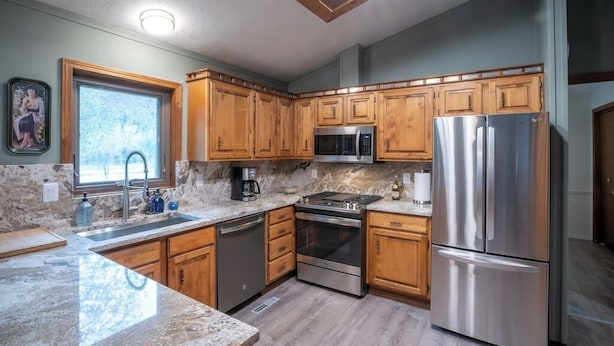 A modern kitchen with wooden cabinets, stainless steel appliances, a granite countertop, and a window with a view.