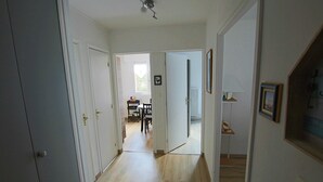 Käytävällä on puulattia, ja se johtaa ruokailutilaan, jossa on pöytä ja tuoleja.