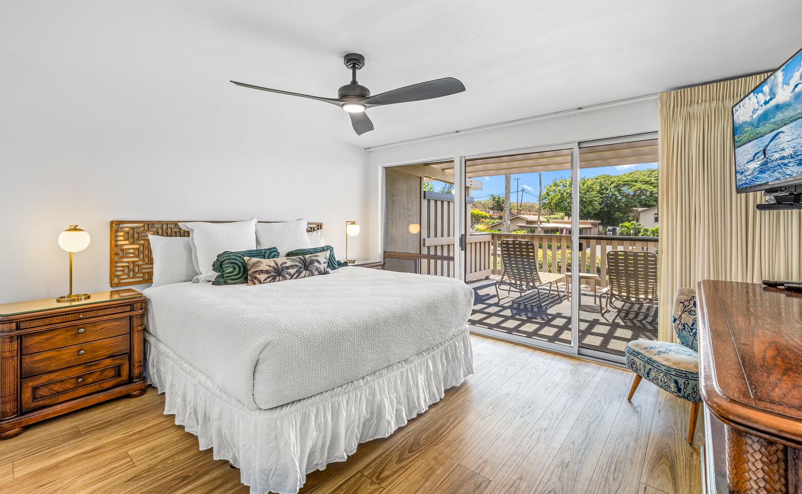 Ein Schlafzimmer mit Bett, Nachttischen, Deckenventilator und einem Balkon mit Gartenmöbeln.