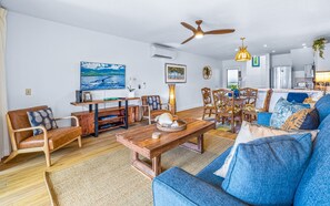 Una sala de estar con una mesa de centro de madera, sofá azul y un comedor con sillas y una mesa.
