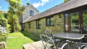 A stone building with a tiled roof and a glass door leading to an outdoor patio with a round table and metal chairs. - The Long Barn for Families, Pets & Workers (Penzance)