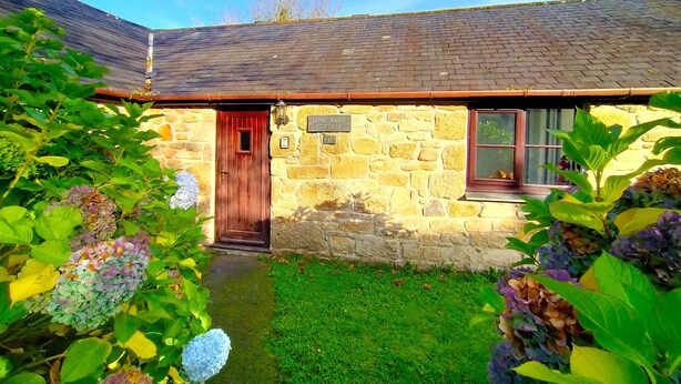 A stone cottage with a wooden door, a small window, and a sign reading "Long Barn Cottage." - The Long Barn for Families, Pets & Workers (Penzance)
