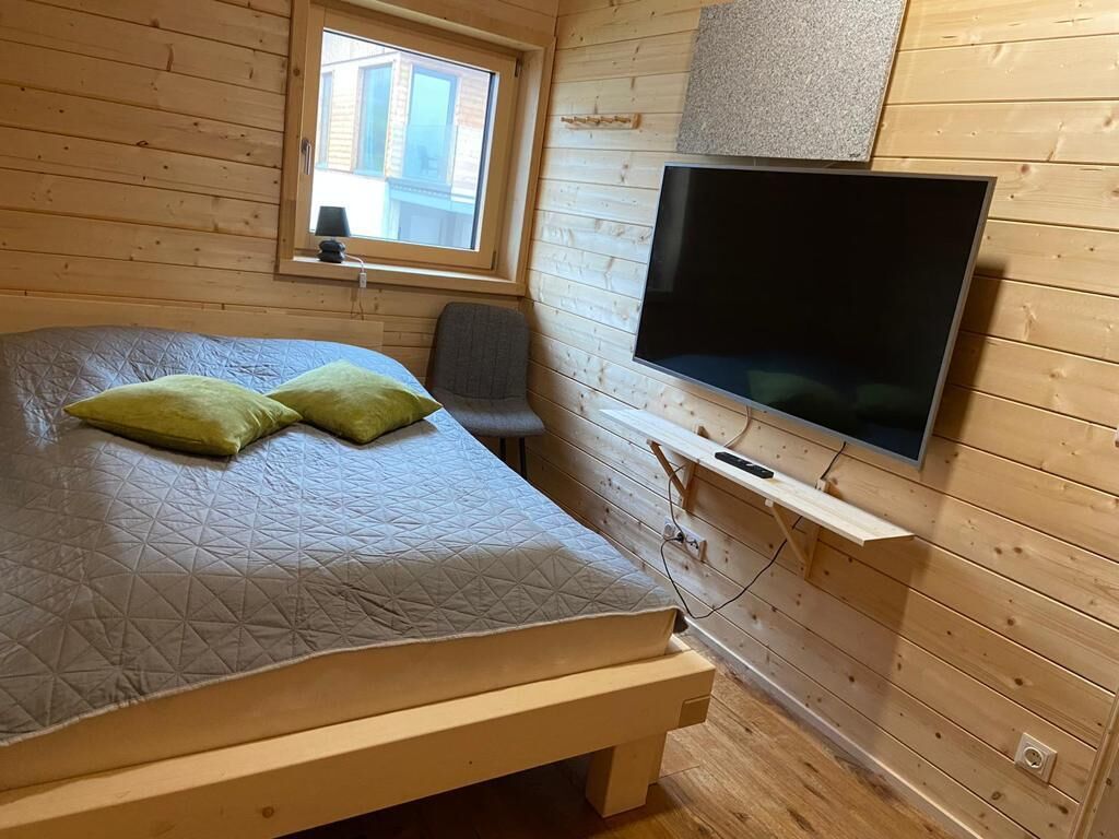 Una habitación tipo cabaña de madera con una cama, una silla, un televisor y una ventana.