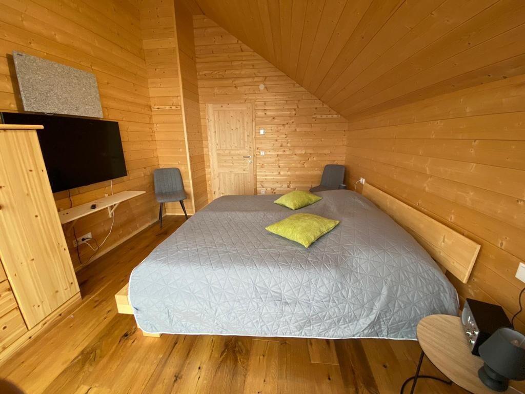 A cozy wooden cabin bedroom with a bed, two pillows, a TV, and a desk with a lamp.