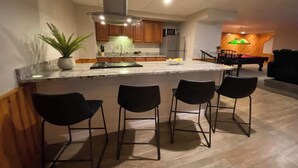 Una cocina moderna con una isla central, taburetes de bar y un comedor con un piano.