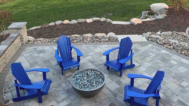 Un patio al aire libre con sillas Adirondack azules, una chimenea y vistas a un estanque y árboles.