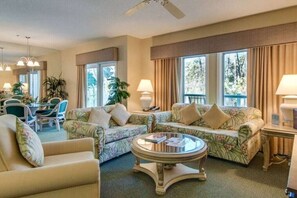 Relax in a comfortable seating area with a sofa and armchairs, dining table, and large windows offering a view of the outdoors.