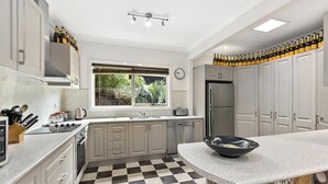 Une cuisine moderne avec un carrelage à motifs, des meubles blancs, un réfrigérateur en acier inoxydable et une fenêtre donnant sur un paysage verdoyant.