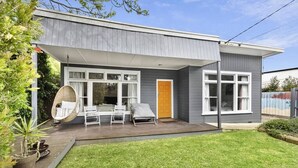 Une maison moderne à deux étages, dotée d’un patio couvert, d’une chaise suspendue et d’un petit jardin.