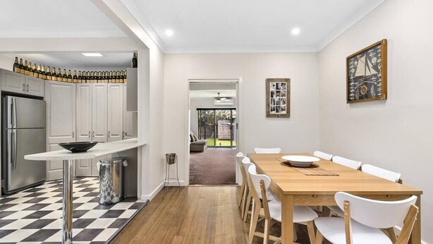 Une cuisine moderne avec un carrelage à motifs, un coin repas avec une table en bois et des chaises blanches, et une vue sur l’espace de vie.