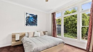 Une chambre avec une grande fenêtre, un lit avec une tête de lit, une table de chevet et une œuvre d’art accrochée au mur.