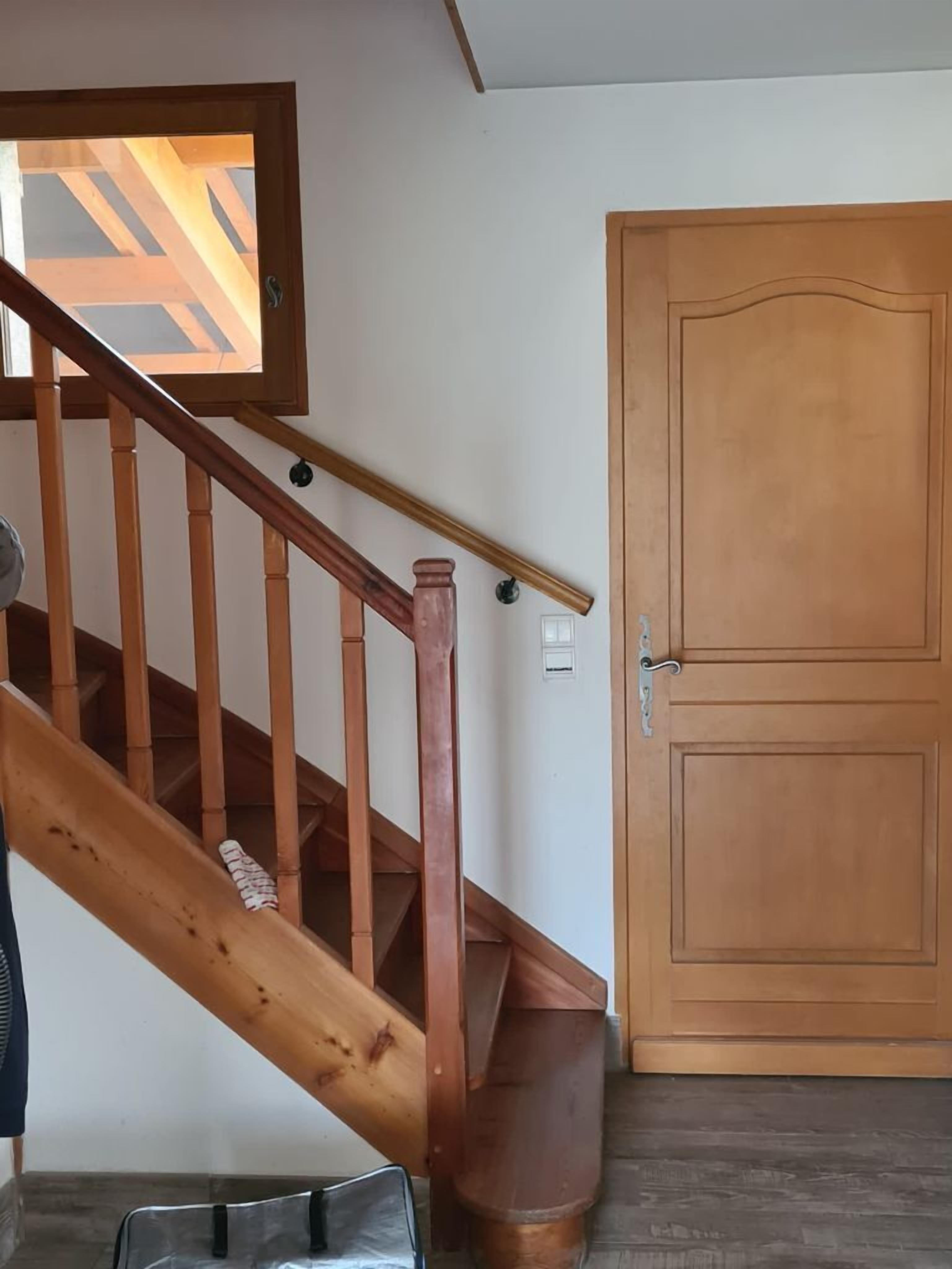 Un escalier en bois avec une rampe, une porte en bois fermée et une fenêtre ornée d’un motif géométrique.