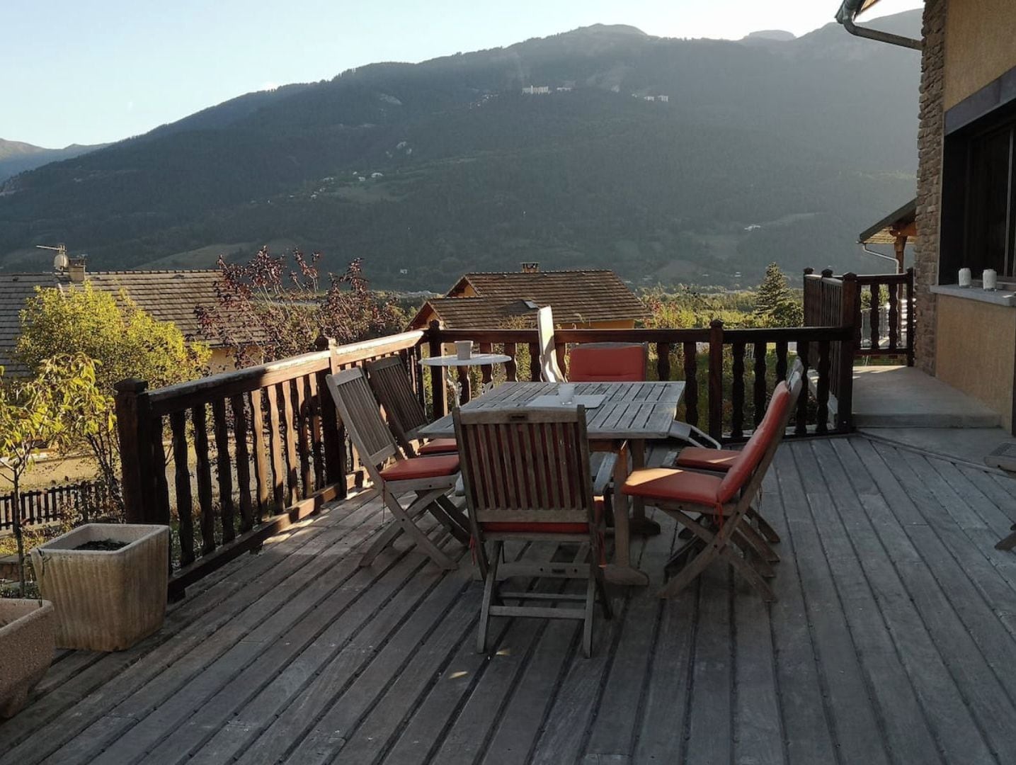 Une terrasse en bois avec une table et des chaises, offrant une vue sur un paysage montagneux.