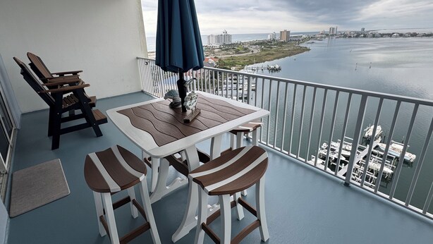 Un balcone con tavolo e sedie, vista sull'acqua e uno skyline sullo sfondo.