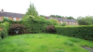A residential garden with a grassy lawn, a hedge, and a brick house in the background. - Inviting 5-bed House in Stockport Bramhall (Stockport)