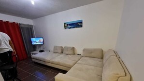 Un saló amb un sofà seccional beig, una televisió de pantalla plana i un quadre a la paret.